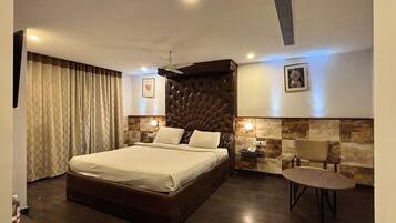 A hotel room with a large bed, a small table, a chair, a nightstand, and a wall-mounted light.