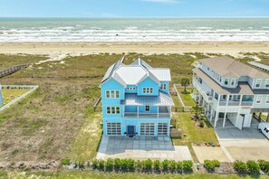 Ein zweistöckiges Strandhaus mit großer Garage, einer überdachten Veranda und Blick auf den Ozean.