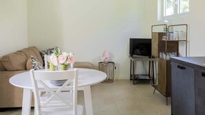 Een woonkamer met een witte tafel, een bank, een televisie en een kast met glazen.