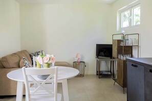 Ein Wohnzimmer mit weißem Tisch, einer Couch, einem Fernseher und einer Vitrine mit Gläsern.