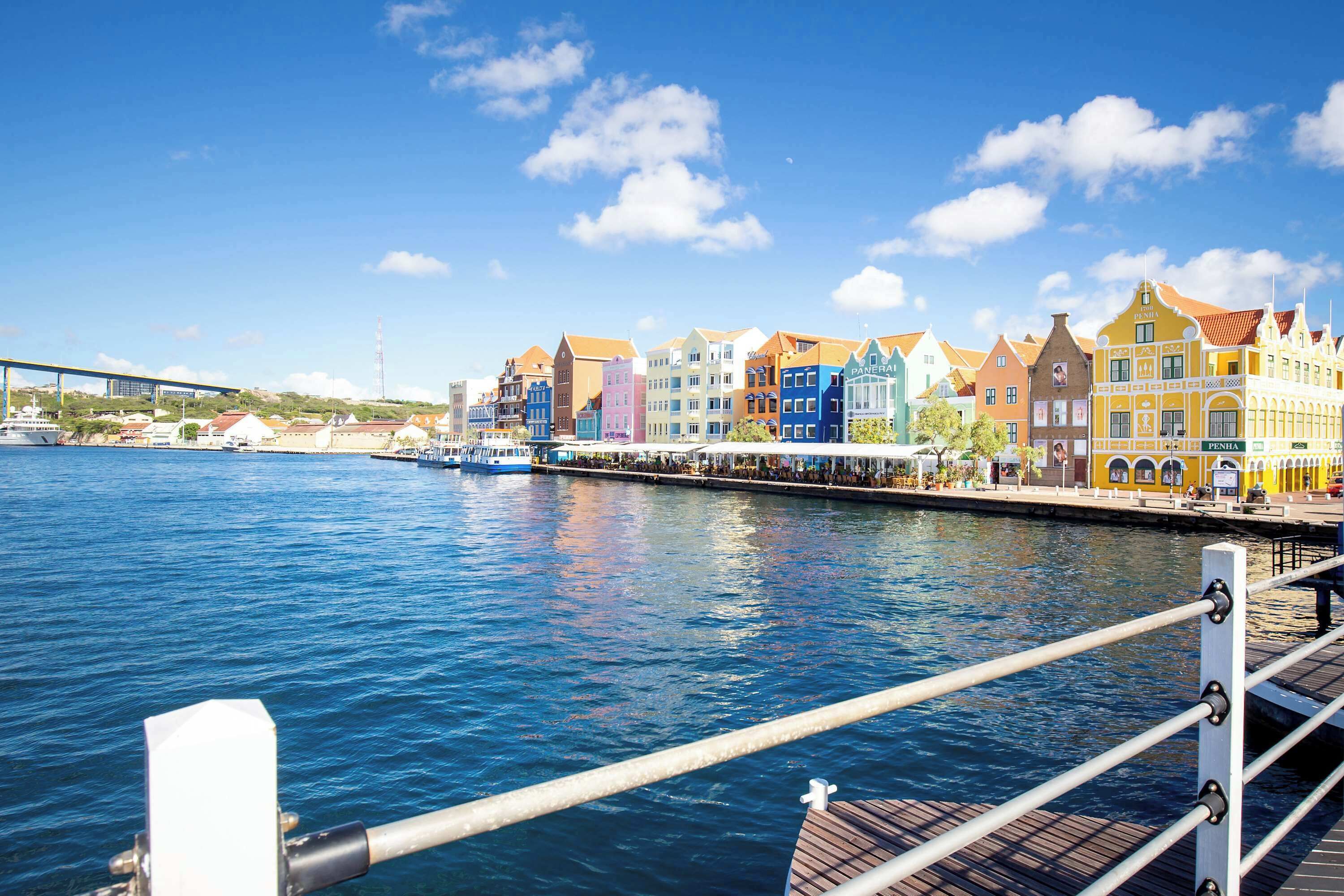 Vista sull'acqua con edifici colorati, un ponte sullo sfondo e cielo azzurro limpido.