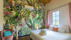 Een slaapkamer met een bed, een stoel, een vaas met bloemen en een wand met tropisch thema.