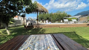Un patio con una mesa de baldosas decoradas, un banco de madera y una estructura de techo de paja.