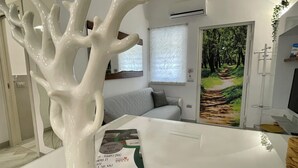 Un interior moderno con una escultura de un árbol blanco, un sofá, un cuadro de un sendero forestal y un libro titulado 'TEMPORARY HOUSE IN VILLAM'.
