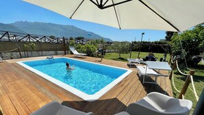 Una piscina con bordo in legno, poltrone da relax e vista sulle montagne.