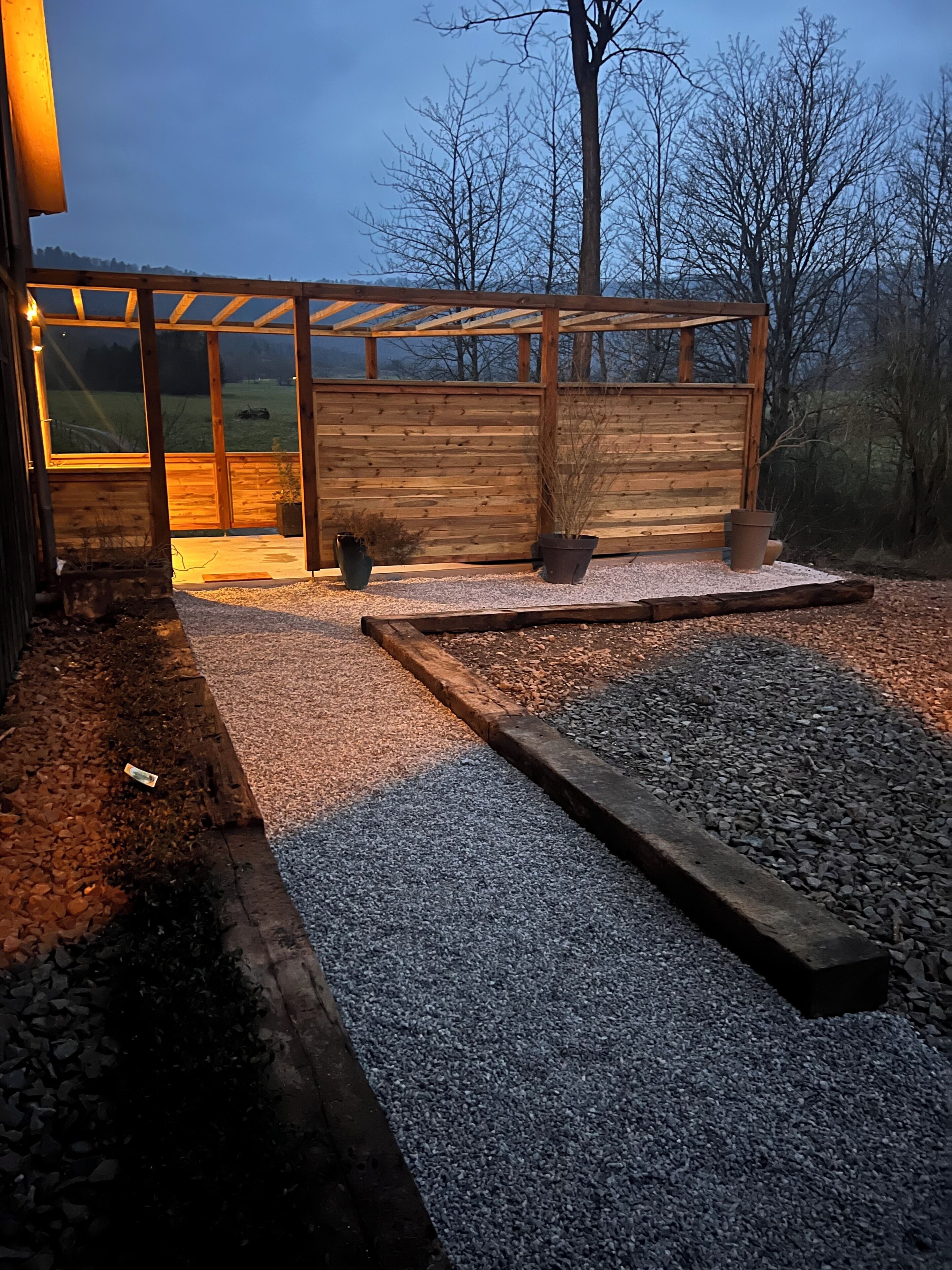 A wooden structure with a glass enclosure, gravel flooring, and potted plants.
