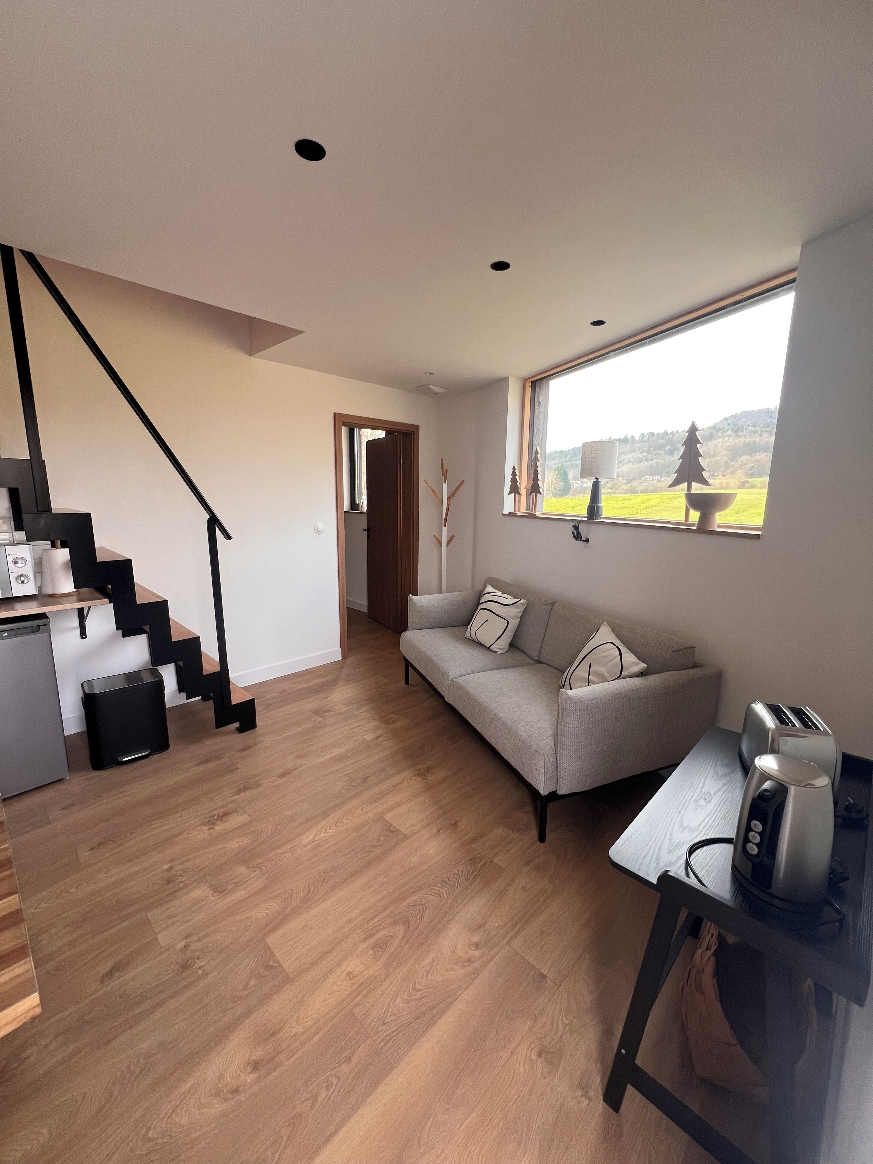 A modern living space with a staircase, a sofa, a dining table, and a view of the outdoors.