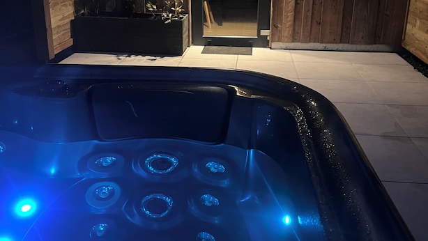 Ett bubbelbad med upplysta munstycken, en yttervägg av trä och en dörr som leder in till ett köksområde.