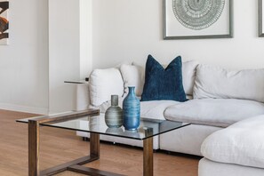 A modern living room with a glass-top coffee table, white sofa, and decorative vases.