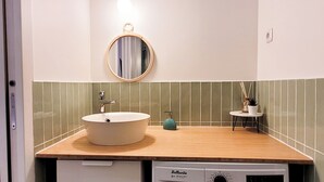 Ein Badezimmer mit einem runden Spiegel, einem Waschbecken und einem kleinen Tisch mit einer Pflanze.