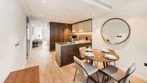 A modern kitchen with a central island, a dining area with a round table, and a large mirror on the wall. - Refined Luxury 2B2B Home – right next to Battersea Power Station (London)