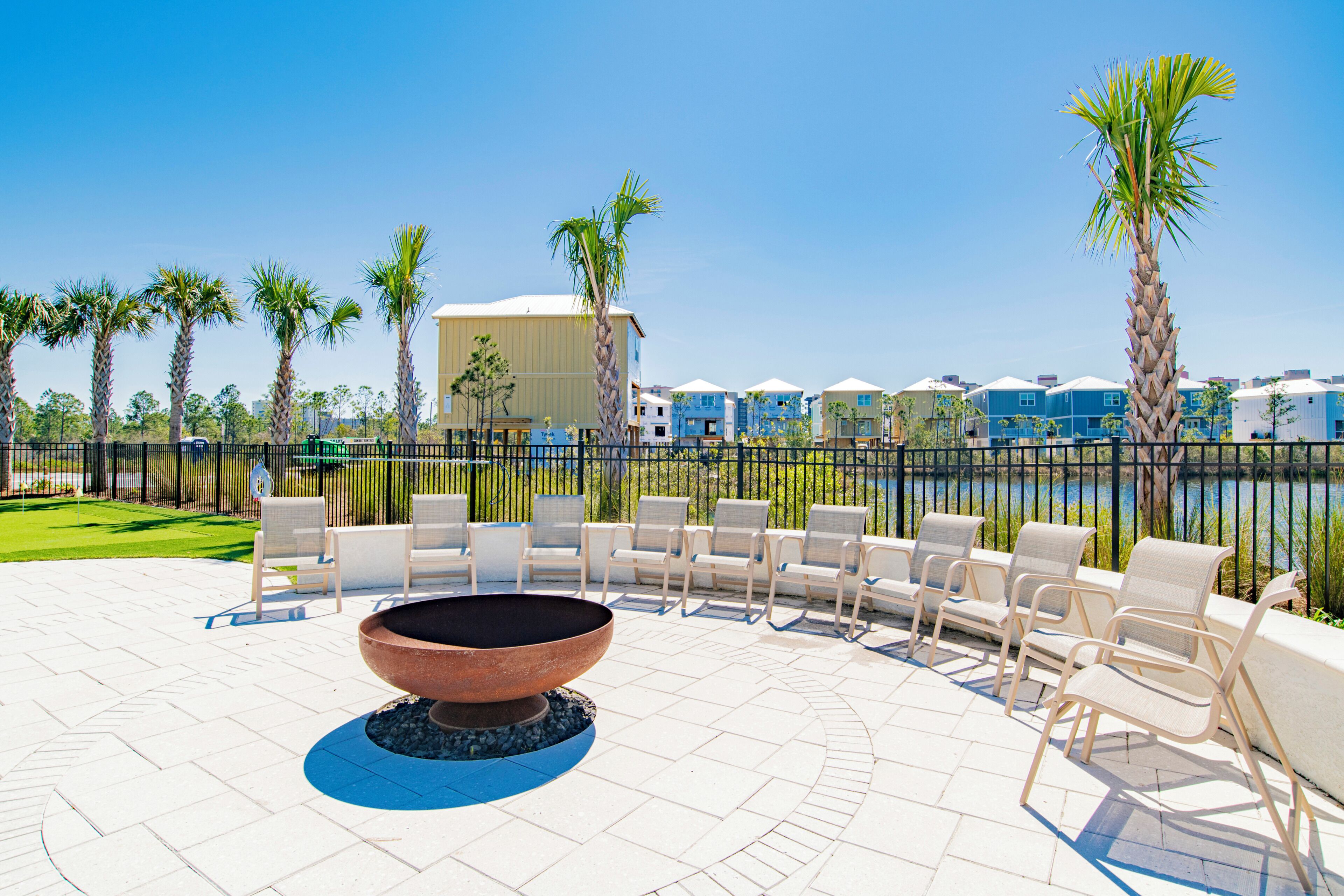 A patio with outdoor seating and a fire pit, surrounded by palm trees and a view of a water body and buildings.