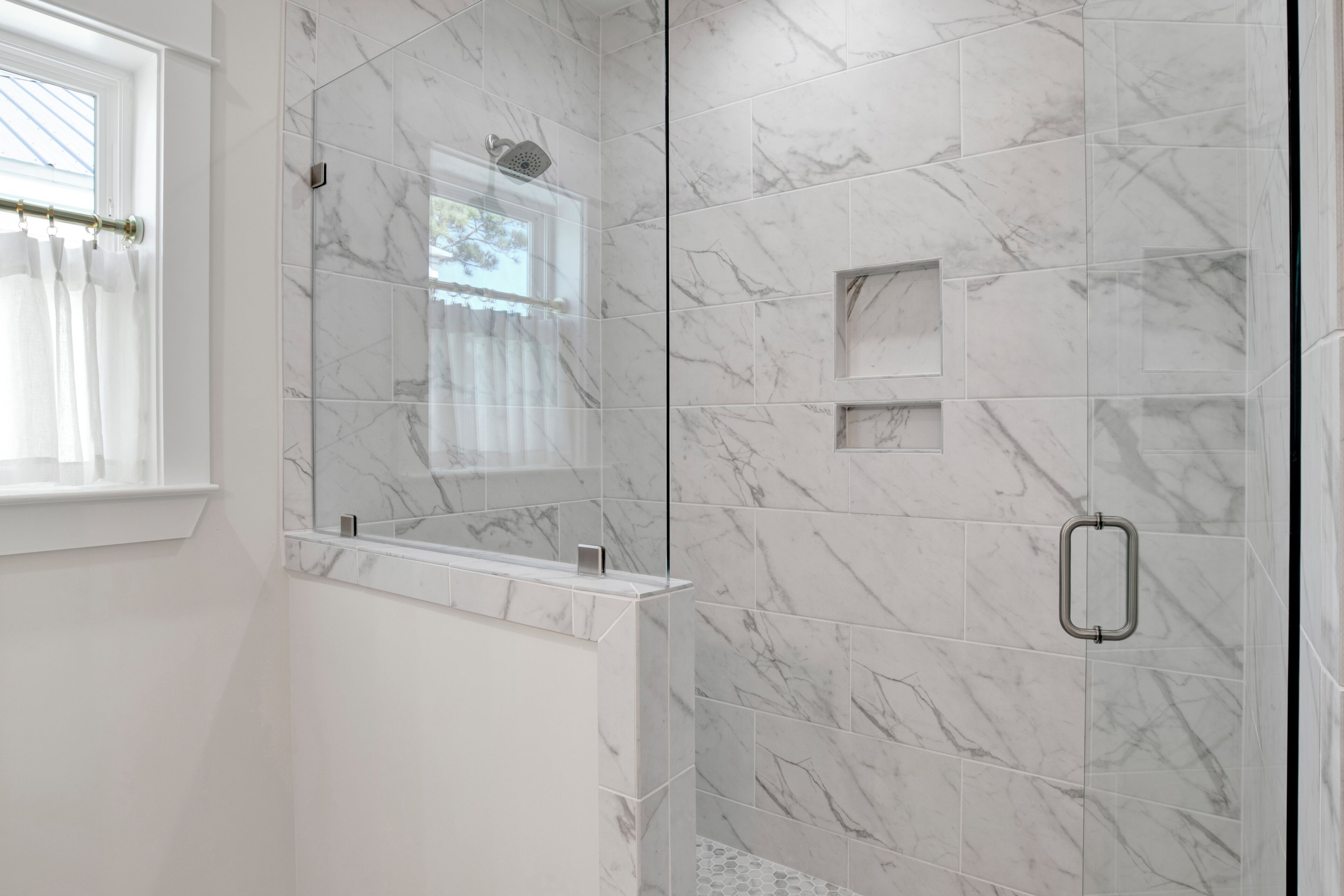 Un baño moderno con cabina de ducha de vidrio, baldosas de mármol y una ventana con cortinas.