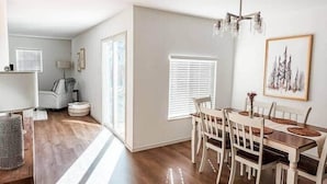 Un comedor amplio con una mesa y sillas de madera, una araña y un cuadro en la pared.