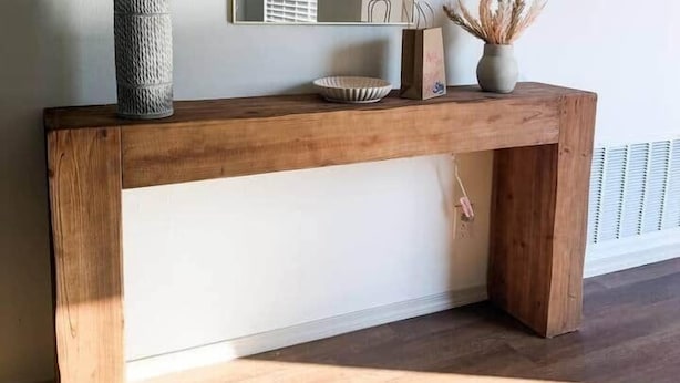 Una consola de madera con una lámpara, un espejo y un florero con plantas secas.