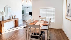 Un comedor con mesa y sillas de madera, una araña y una ventana con persianas.