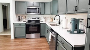 Una cocina moderna con armarios grises, electrodomésticos de acero inoxidable y encimera blanca.