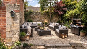 A cozy outdoor seating area with wicker furniture, a stone wall, and a barbecue grill. - Serenity - Cinema, gym, private wellness suite, Painswick (Painswick)