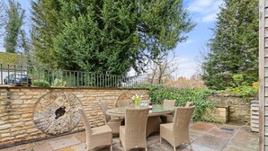 Eine Terrasse im Freien mit einem runden Tisch und Korbstühlen, umgeben von Steinmauern und Grünpflanzen.