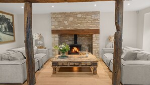 Ein gemütliches Wohnzimmer mit einem Kamin aus Stein, zwei grauen Sofas, einem Holztisch und einem Gemälde an der Wand.