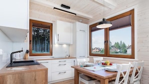 A modern kitchen with wooden cabinets, a sink, and a dining area with a table and chairs. - Comfortable Holiday Home , Summer Pool (Rewal)