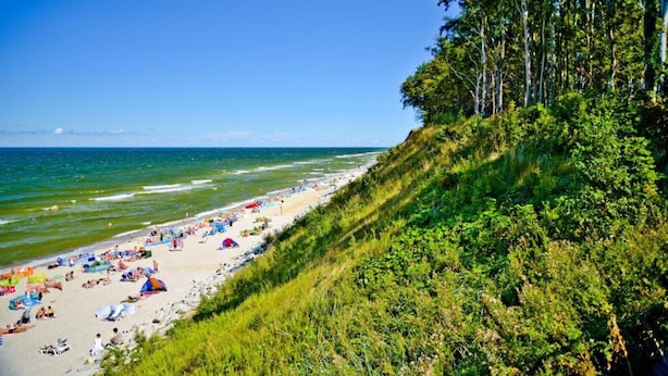 A beach with people, umbrellas, and a grassy cliff. - Comfortable Holiday Home , Summer Pool (Rewal)