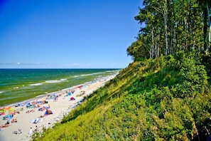 A beach with people, umbrellas, and a grassy cliff. - Comfortable Holiday Home , Summer Pool (Rewal)