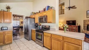 A kitchen with wooden cabinets, a refrigerator, a microwave, a stove, and a dining area with chairs. - Aviation Retreat +Pool +Sunset Views (Oro Valley)