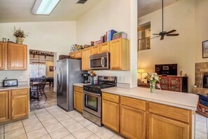 A kitchen with wooden cabinets, a refrigerator, a microwave, a stove, and a dining area with chairs. - Aviation Retreat +Pool +Sunset Views (Oro Valley)