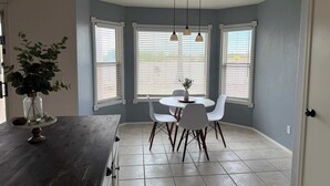 A dining area with a table and chairs, a potted plant, and a window with blinds. - Aviation Retreat +Pool +Sunset Views (Oro Valley)