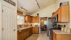 A kitchen with wooden cabinets, a microwave, a stove, and a dining area with a table and chairs. - Aviation Retreat +Pool +Sunset Views (Oro Valley)