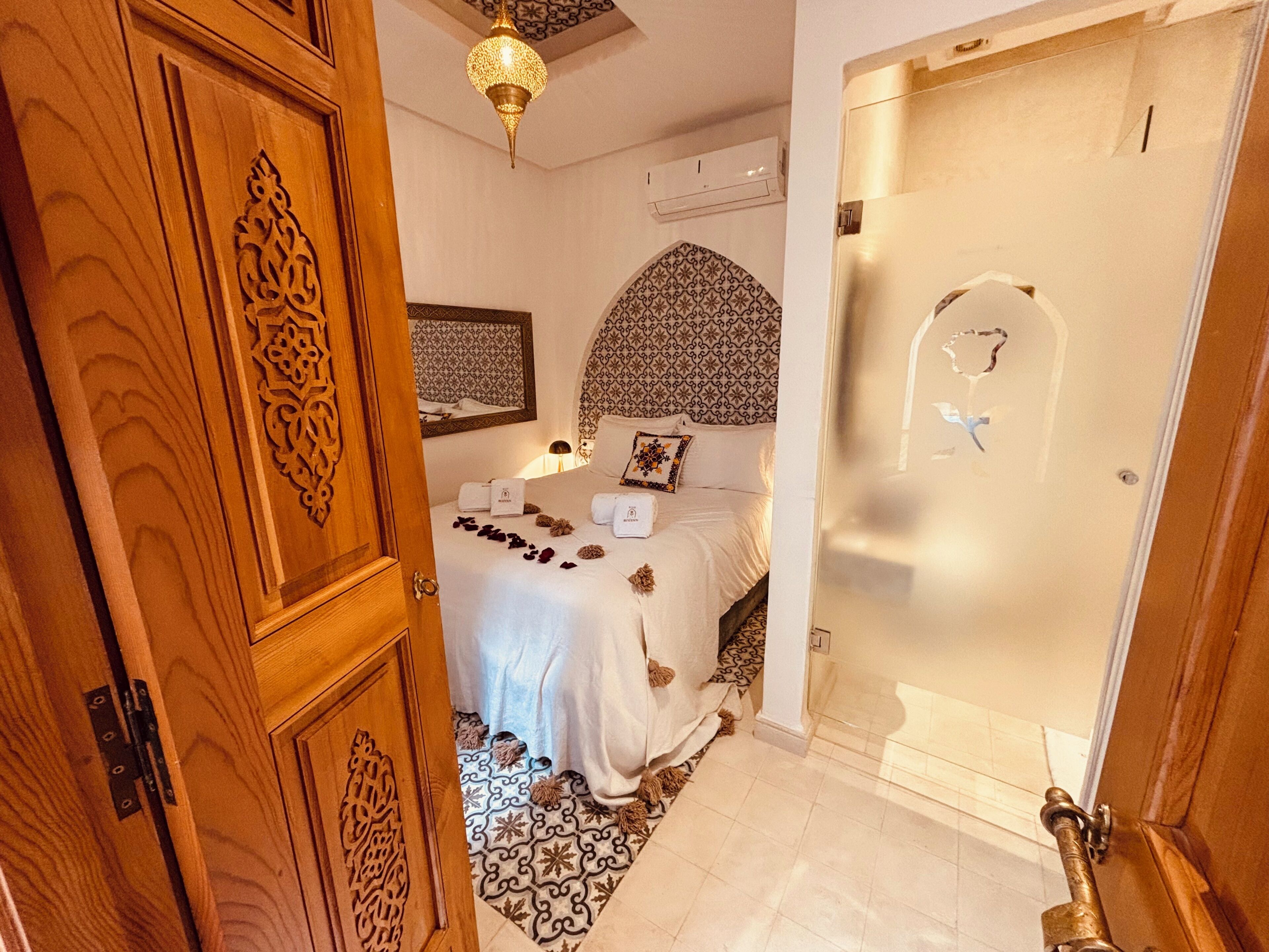 Une chambre avec un lit, une tête de lit à motifs, un luminaire suspendu et une porte dotée d’une poignée décorative.