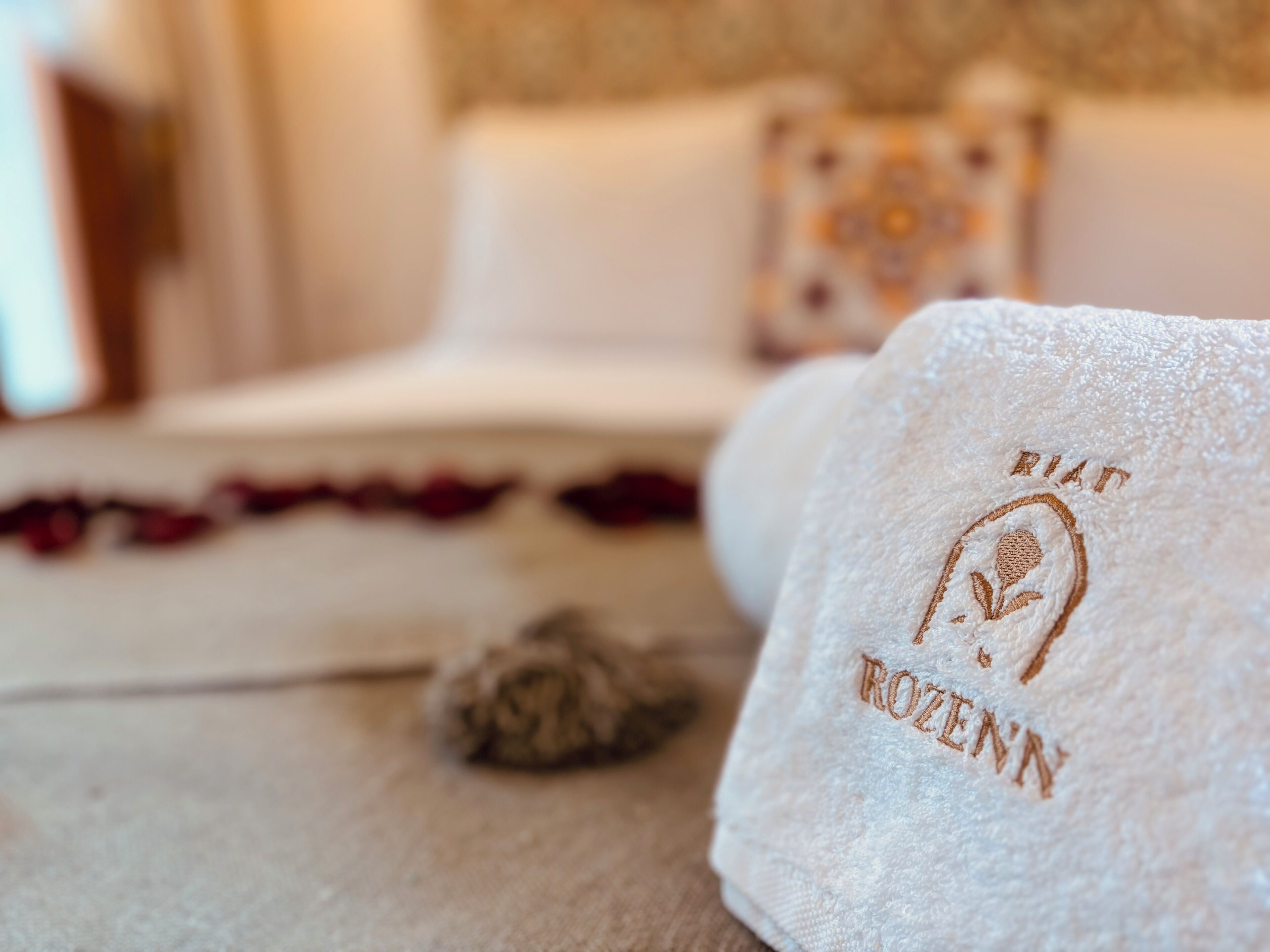 A neatly made bed with a white towel featuring embroidered text, a decorative pillow, and a small decorative item on the bed.