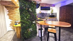 A modern kitchen with a wooden table, bar stools, a brick accent wall, and a vertical garden. - Jacuzzi relaxation near Colmar (Bergheim)