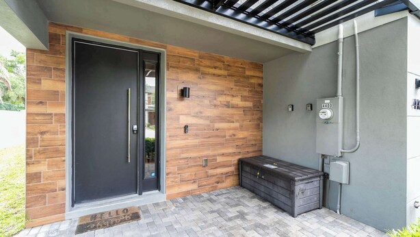 A modern building entrance with a wooden wall, a black door, and a utility box. - Premium Location Near Disney with Pool at Le Reve (Kissimmee)