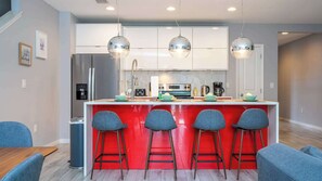 Uma cozinha moderna com ilha central, banquetas, eletrodomésticos de aço inoxidável e iluminação pendente.