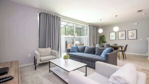 A modern living room with a sofa, armchairs, a coffee table, and a dining area with a table and chairs. - Premium Location Near Disney with Pool at Le Reve (Kissimmee)