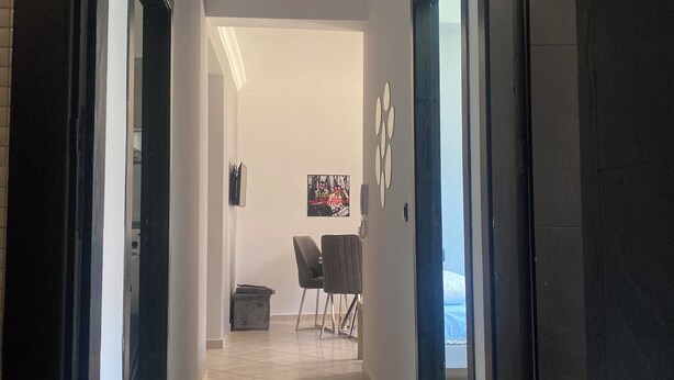 A hallway with a tiled floor, a door on the right, and a chair in the distance. - Woven Calm • 2BR Near Beach, Gateway to Chefchaouen (Martil)