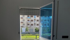 A room with a bed, a window, and a view of a building and greenery outside. - Woven Calm • 2BR Near Beach, Gateway to Chefchaouen (Martil)