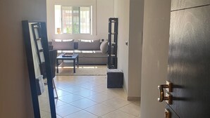 A hallway leading to a living room with a sofa, a coffee table, and a bookshelf. - Woven Calm • 2BR Near Beach, Gateway to Chefchaouen (Martil)
