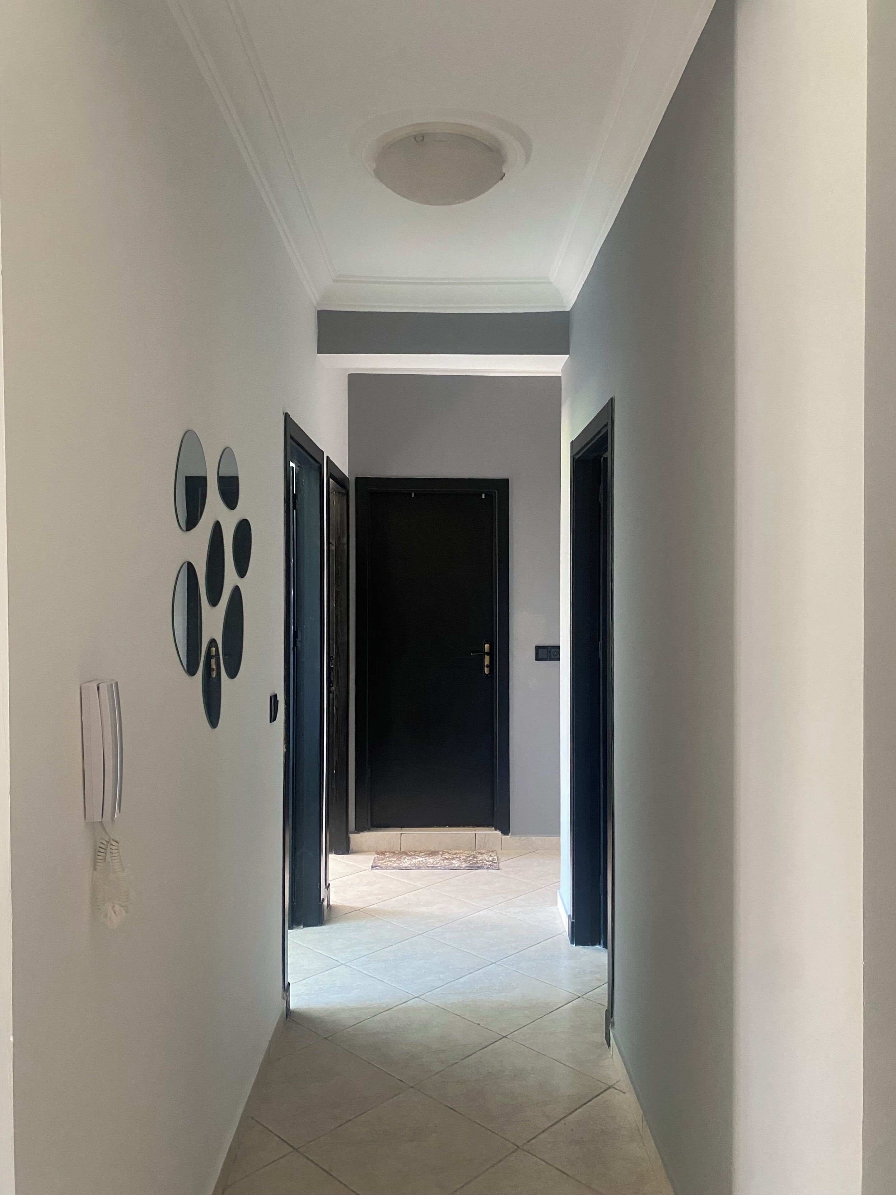 A hallway with a black door at the end, a light switch, and a wall-mounted light fixture.