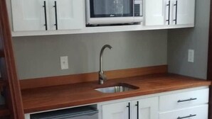 Une cuisine compacte avec des meubles blancs, un four à micro-ondes, un lave-vaisselle et un plan de travail en bois.