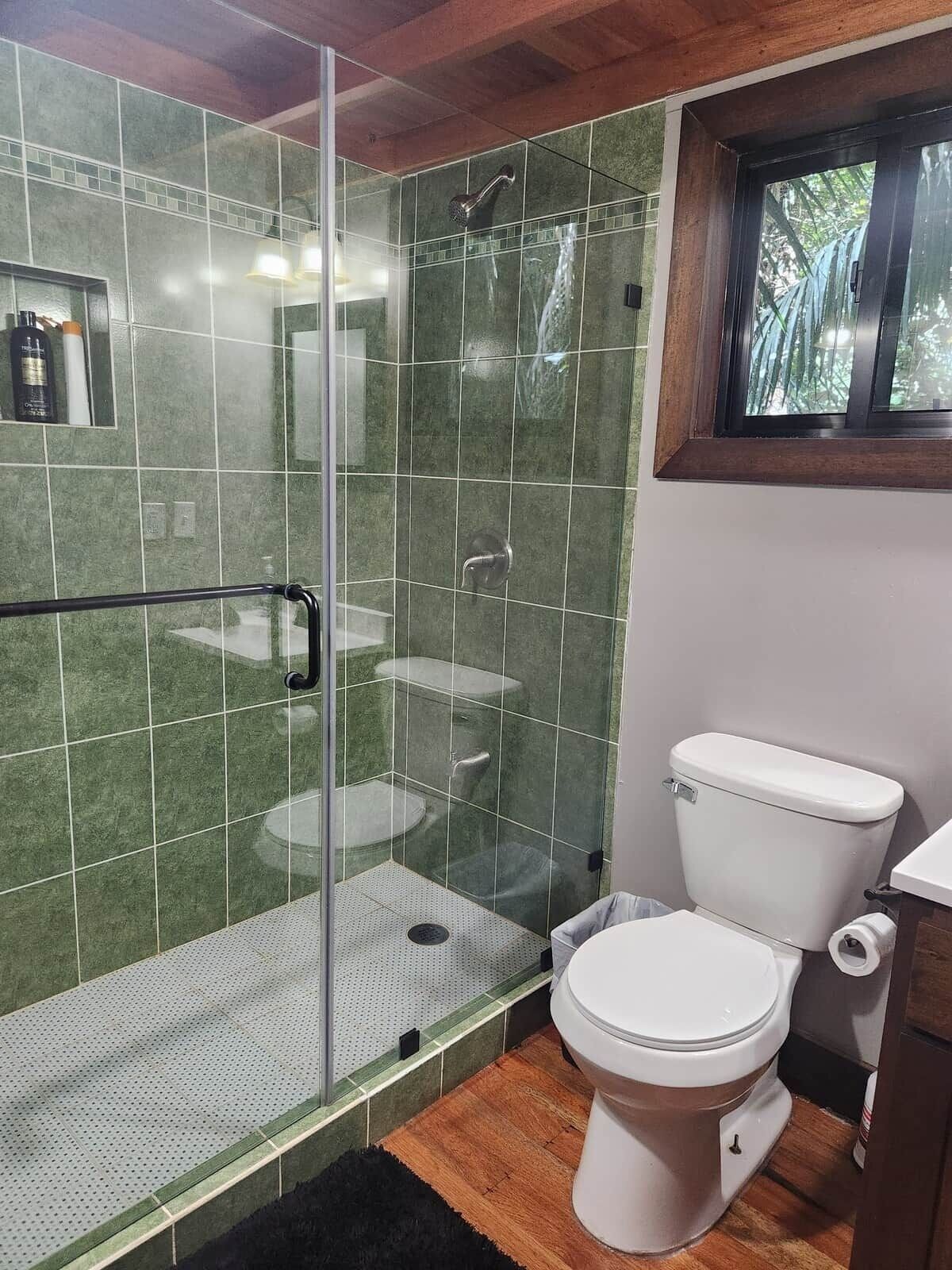 Un baño con ducha de vidrio, inodoro blanco y ventana.