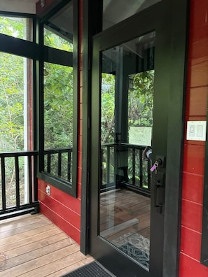 A wooden deck with a glass door leading to a room with a view of greenery.
