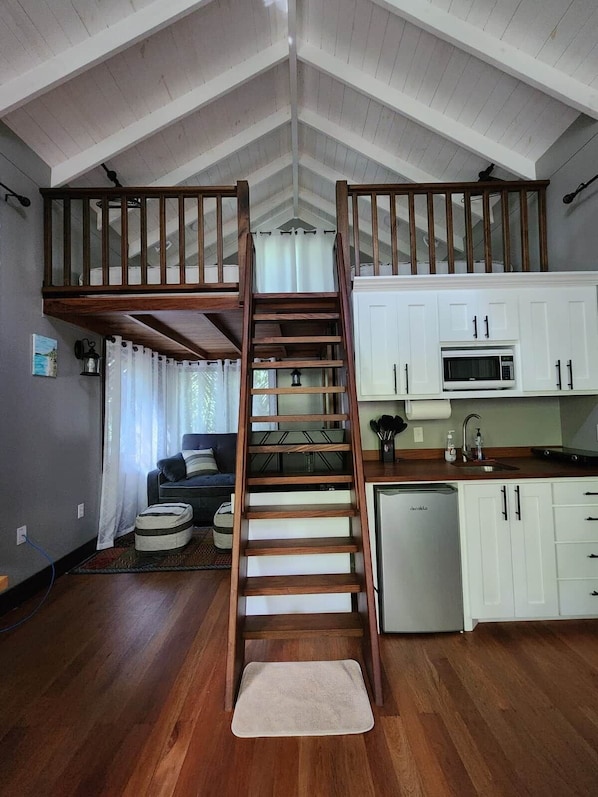 A loft-style room with a wooden staircase, a kitchen with white cabinets, and a dining area with a couch.