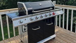 Un barbecue portatif doté de plusieurs brûleurs, dont un brûleur latéral, placé sur une terrasse en bois.