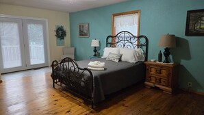 Une chambre à coucher comprenant un lit, une table de chevet, une lampe, un ventilateur de plafond et une fenêtre avec des stores.