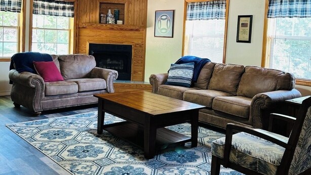 Un salon chaleureux avec un plafond en bois, une cheminée, deux canapés, une table basse et un tapis à motifs.