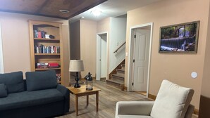 Un salon avec un canapé, un fauteuil, une bibliothèque, une lampe et un tableau accroché au mur.