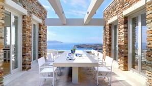 A stone-clad outdoor dining area with a table set for four, overlooking a coastal landscape. - Stone Villa with Panoramic Sea Views over Mylopotas, Ios (P842+3W Chora)